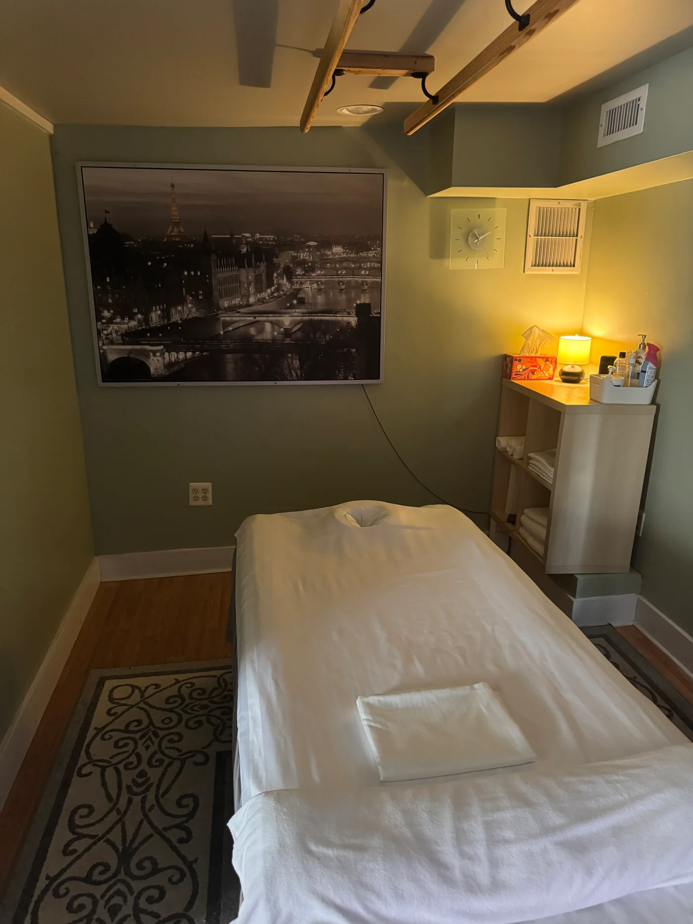Prepared massage table with white linens, a warm lamp and a cityscape wall print at Wellness Foot Spa in Glenside, PA
